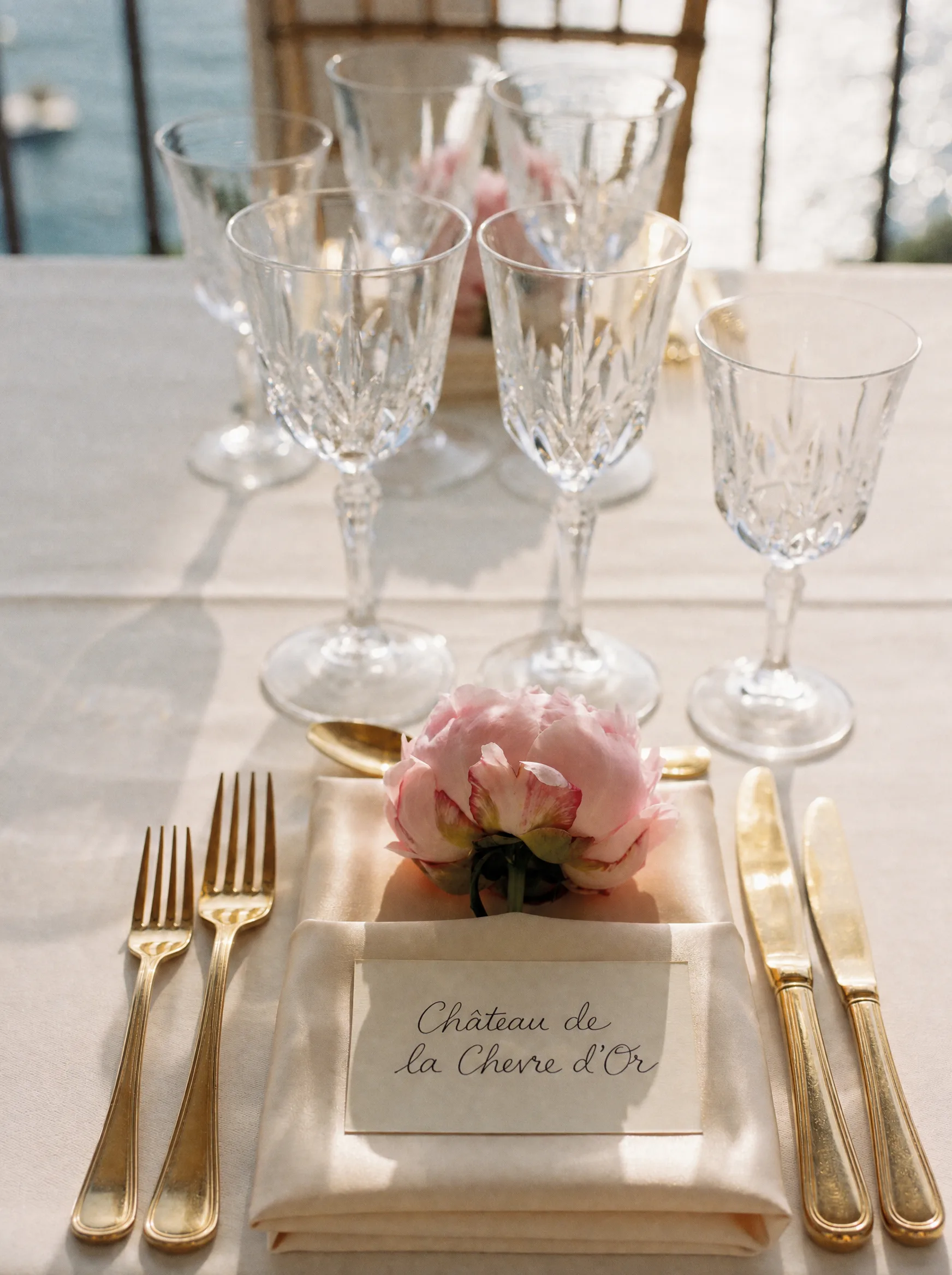 Dressage de table de mariage : cristal taillé, couverts dorés et pivoine poudrée sur lin ivoire, face à la mer